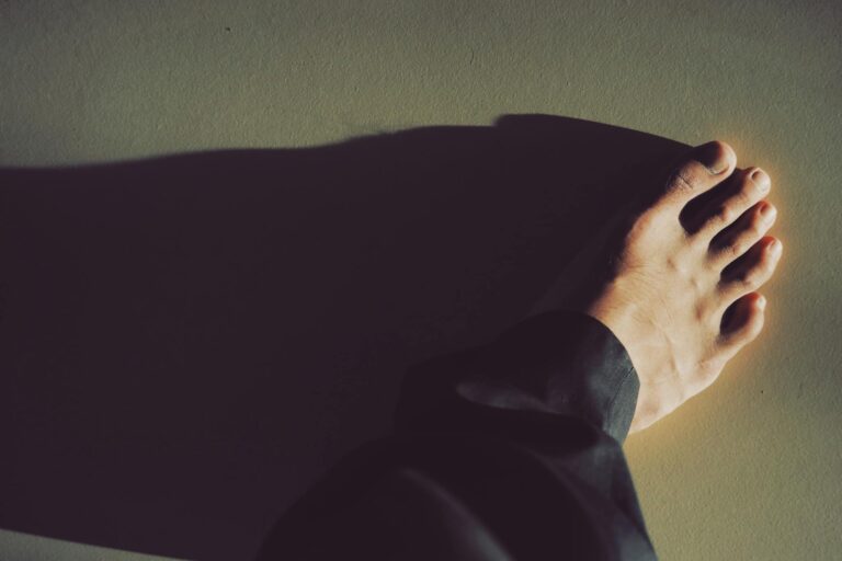 A close-up photo capturing a bare foot casting a dramatic shadow on the ground.