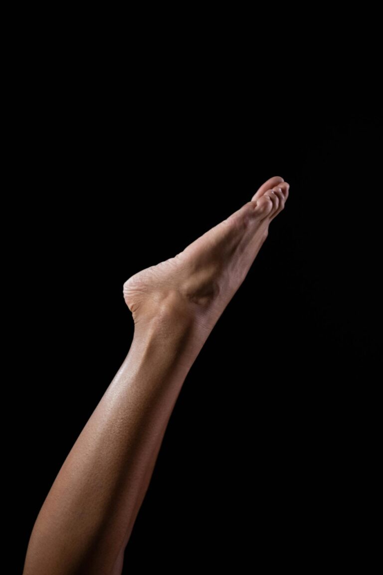 Artistic vertical shot of a woman's leg in studio, highlighting minimalist elegance against a black background.